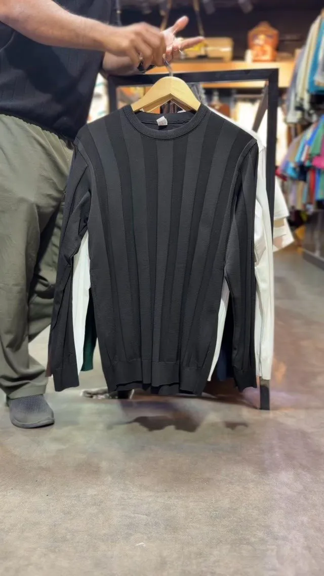 Black crew-neck knit with wide vertical ribs on a wooden hanger in the store