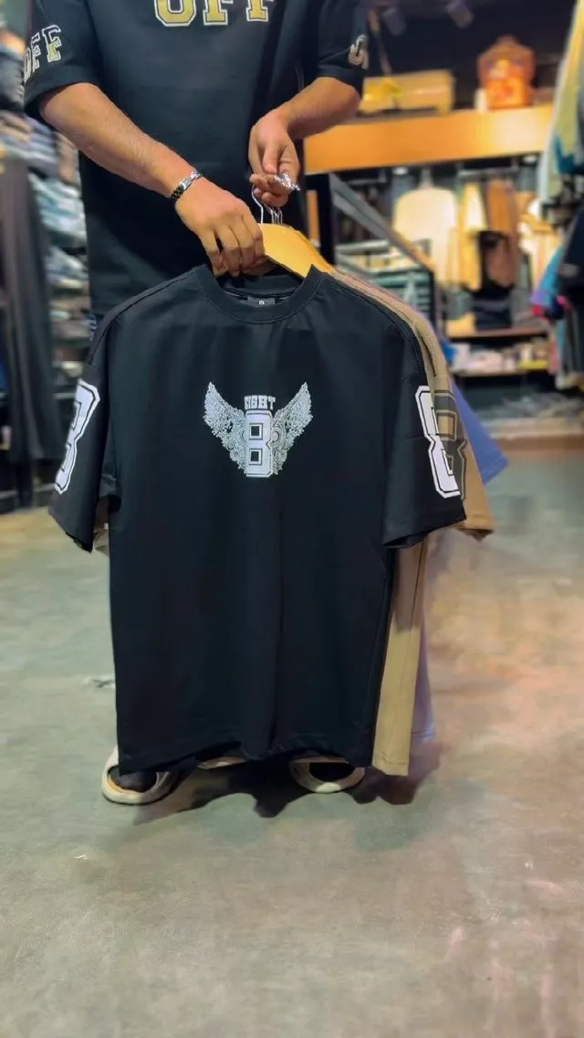Black oversized tee with a winged eight print on a wooden hanger in the store